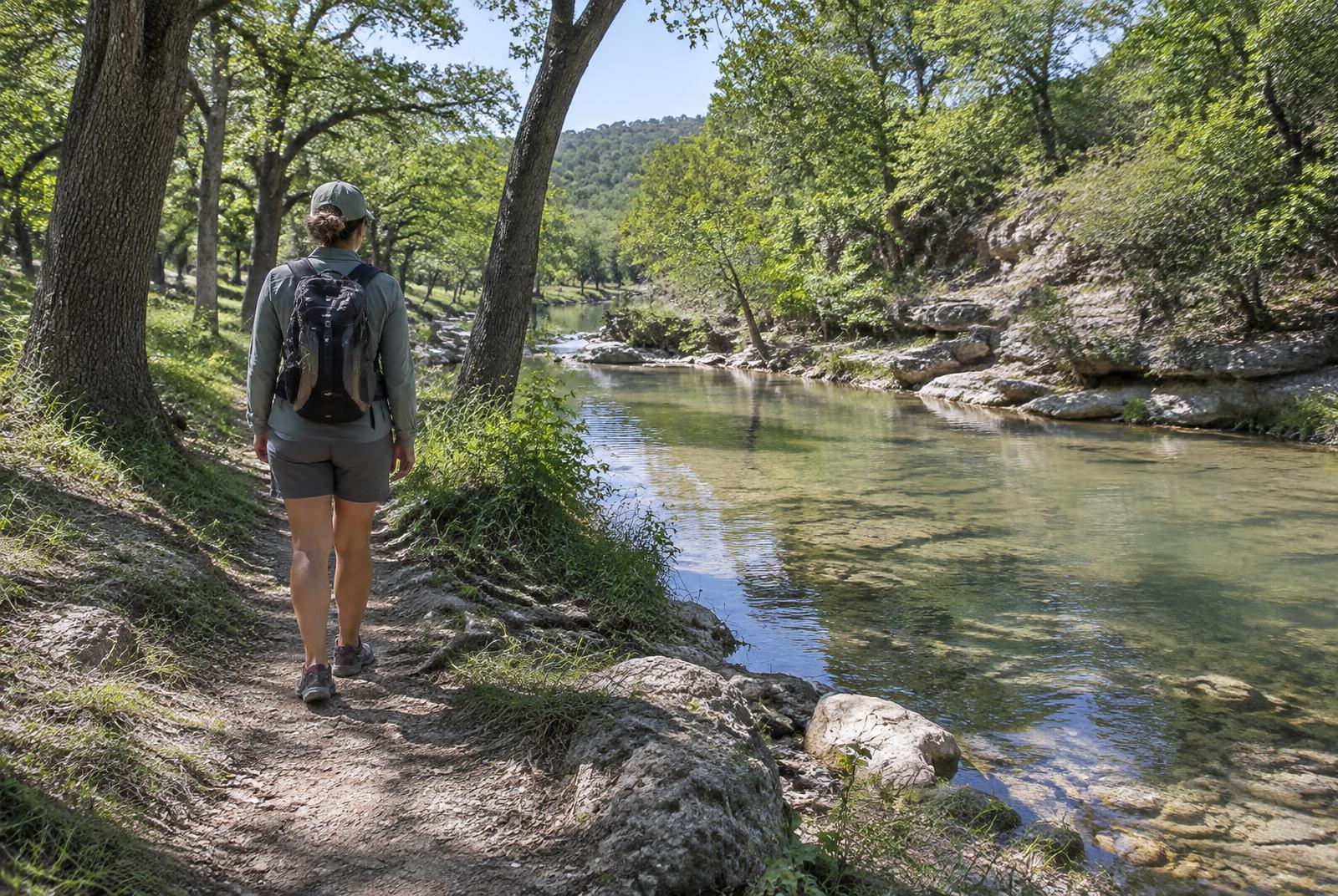 An adult walking beside clear water under live oaks