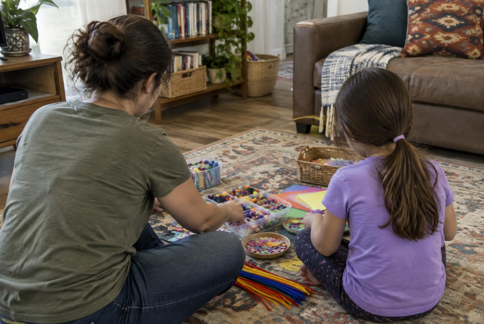 A parent and child sorting colorful craft materials on the floor