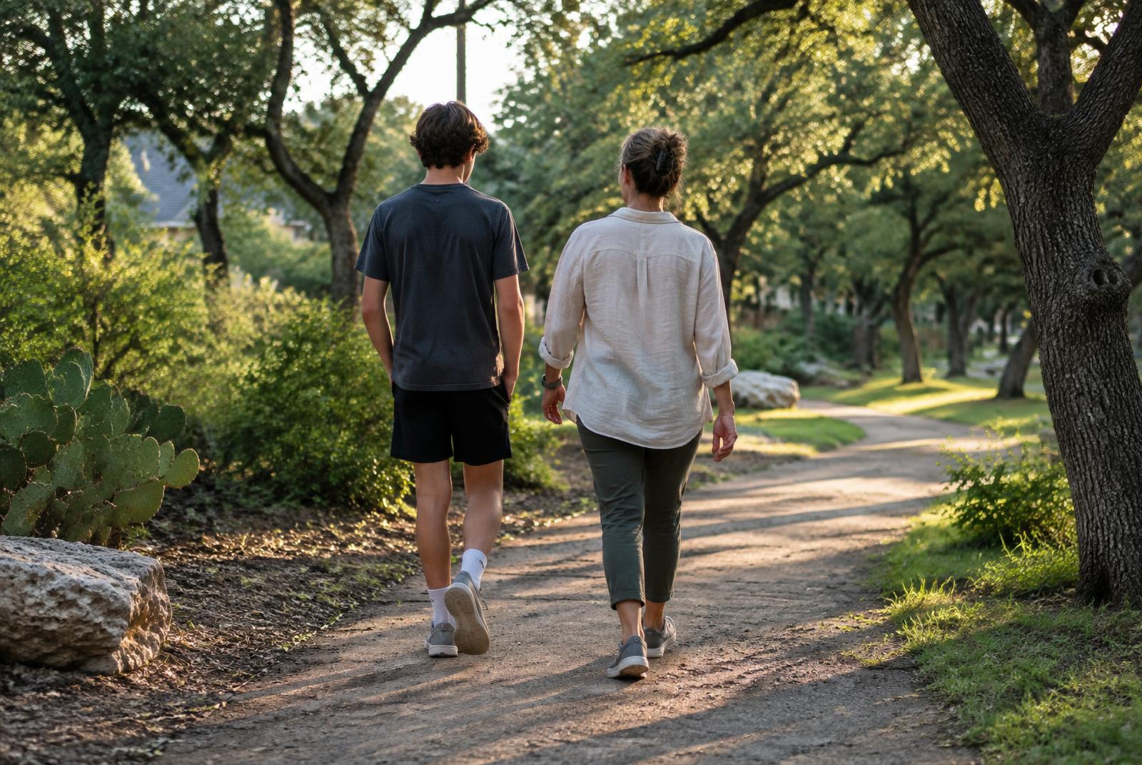 A parent and teen walking together along an oak-shaded path